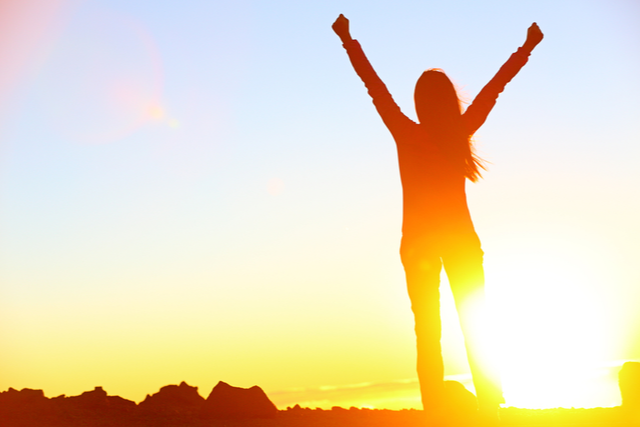 Woman celebrates a win with hands in the air facing the rising sun