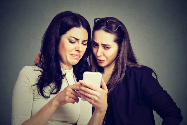 Two women looking at a smartphone with disgusted facial expressions