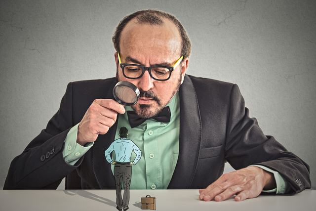 Man in mid-50s holding a magnifying glass over a cartoon drawing of a man on a suit